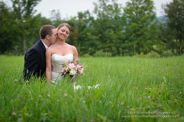 Bride & Groom sitting in hay field, groom kissing bride's neck