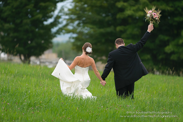 Bride & Groom walking in hay field, groom holding bouquet in air