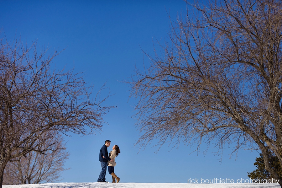 couple at engagement session on top of hill with blue sky in background