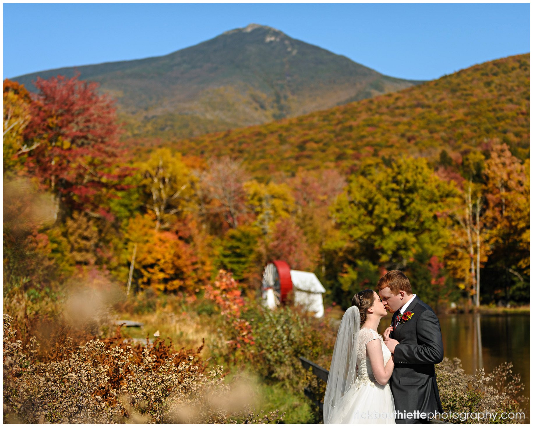 bride and groom kissing with waterwheel in background with fall colors at Indian Head Resort wedding