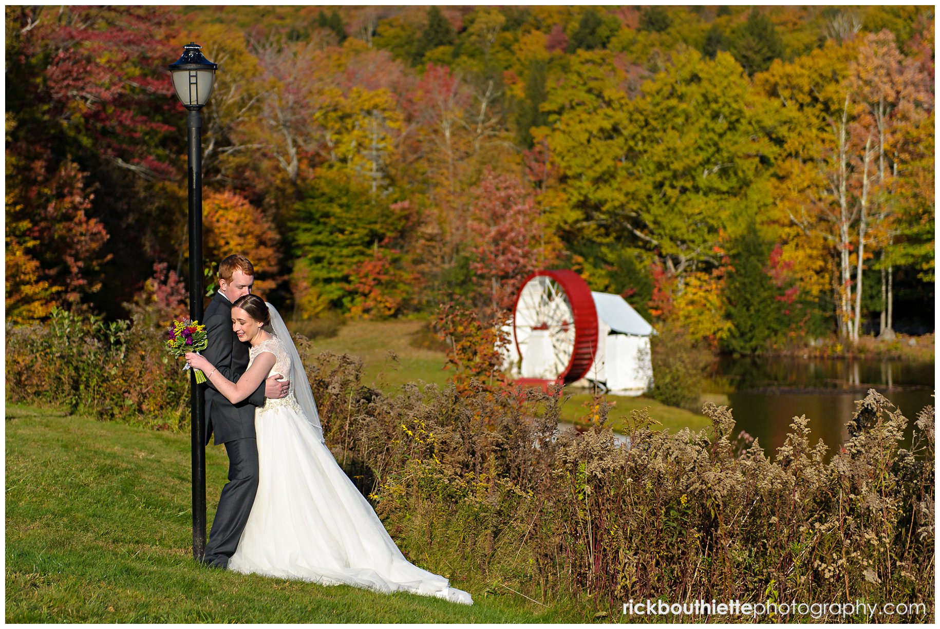 bride and groom embrace with waterwheel in background at fall Indian Head Resort wedding