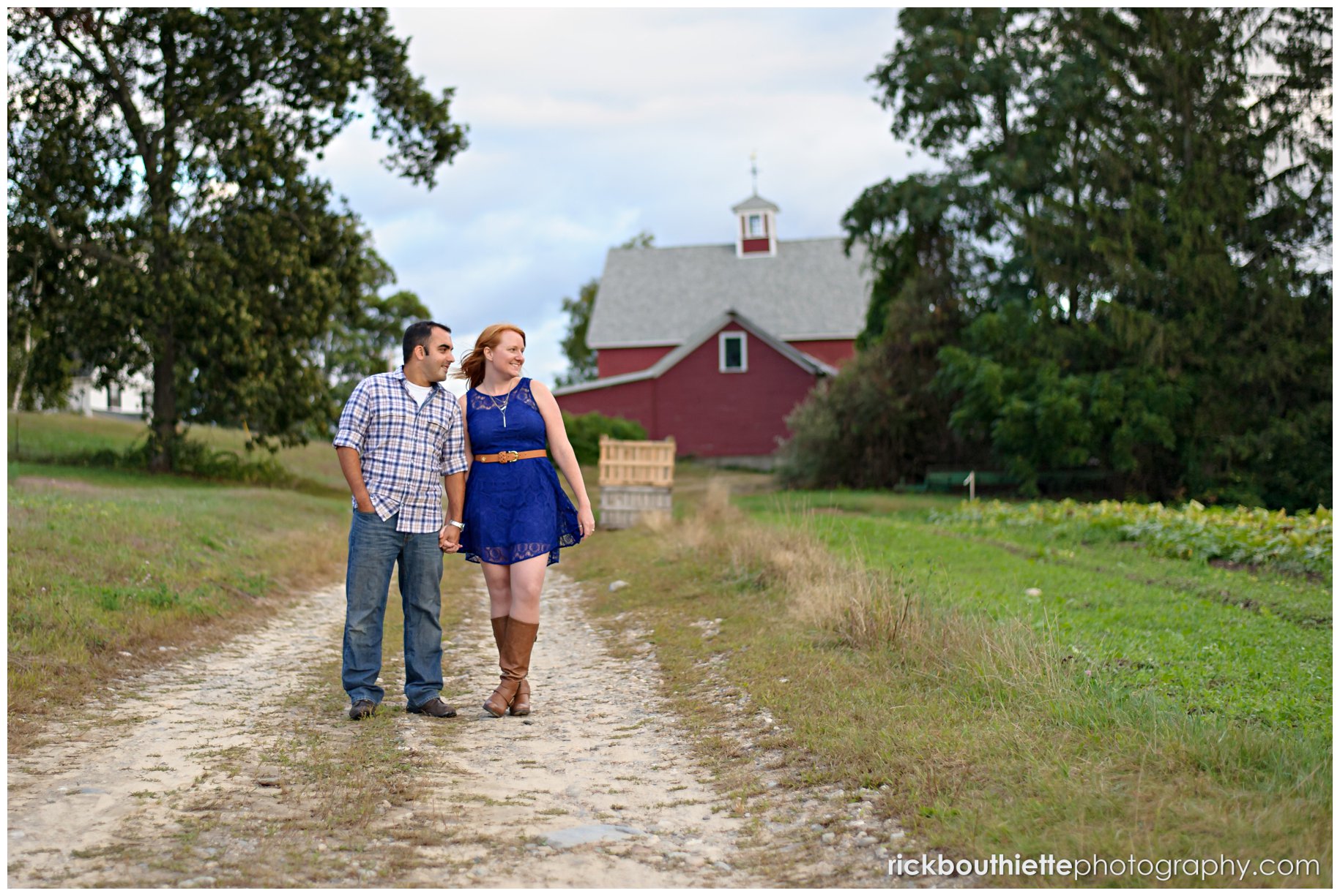 couple walking on gravel road with red barn in background during engagement session