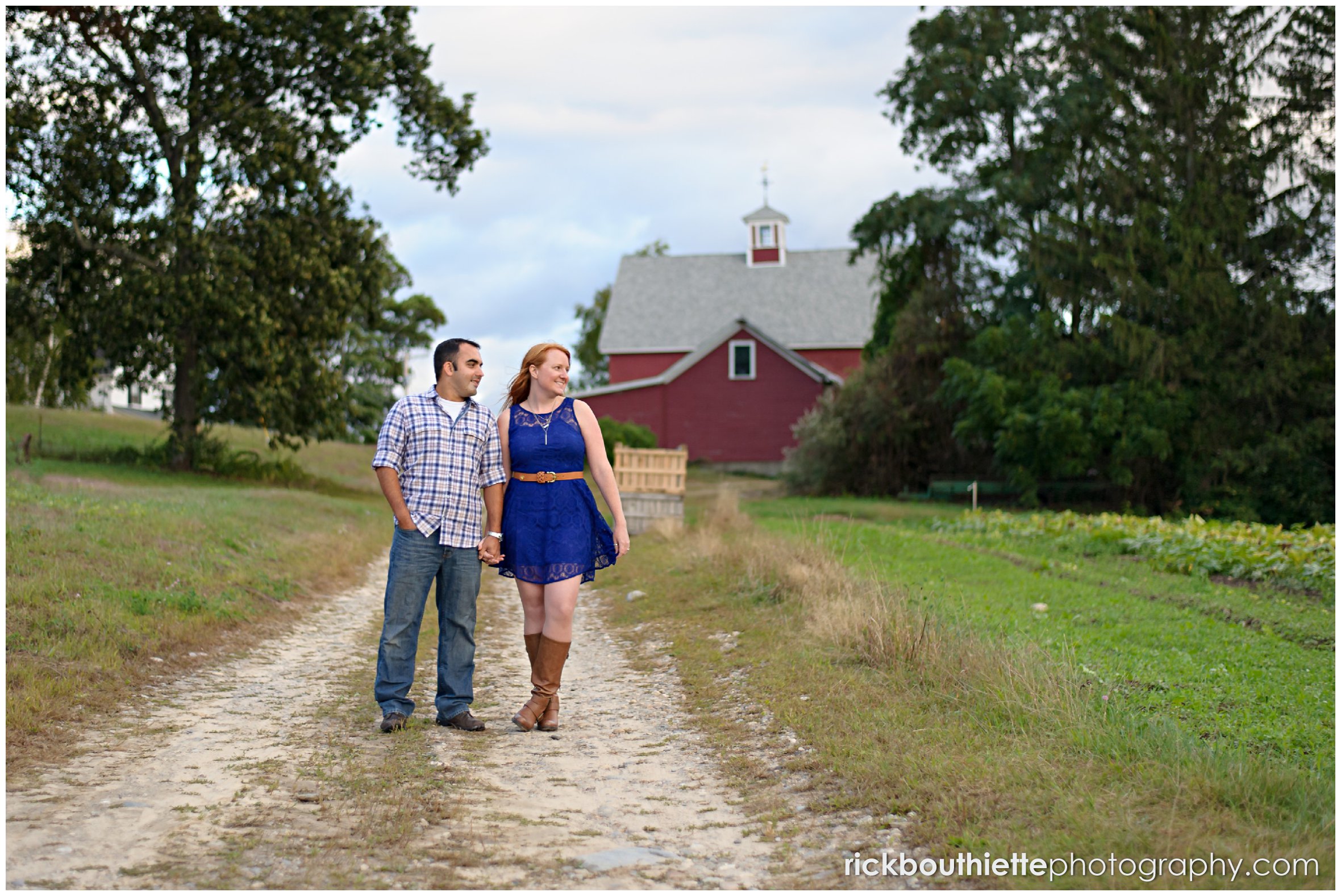 couple walking down road with red barn in background during engagement session