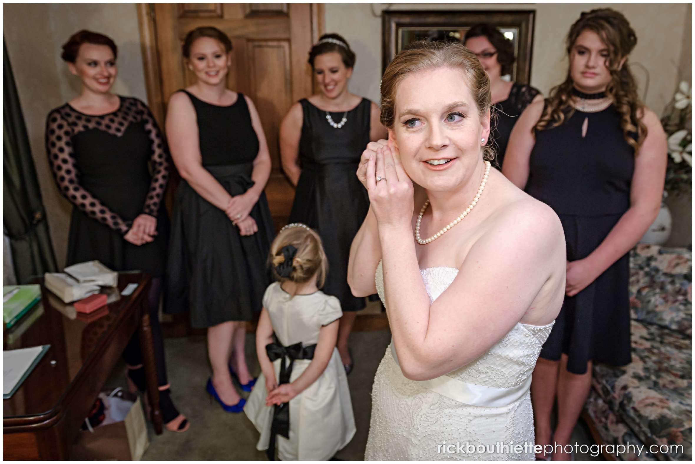 bride putting her earrings on with bridesmaids in the background