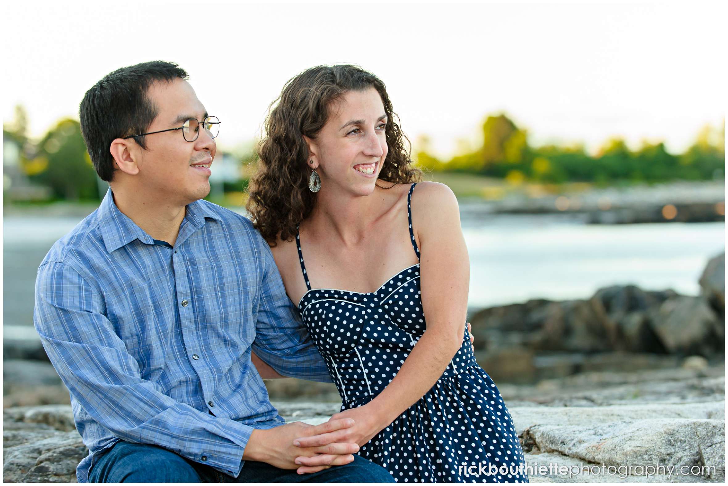 couple gazing out to the ocean while sitting on the rocks near the beach at Great Island Common engagement session