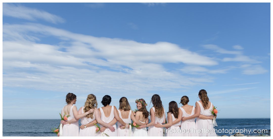 bride and bridesmaids look out to ocean with arms around each other at New Hampshire Seacoast Science Center wedding
