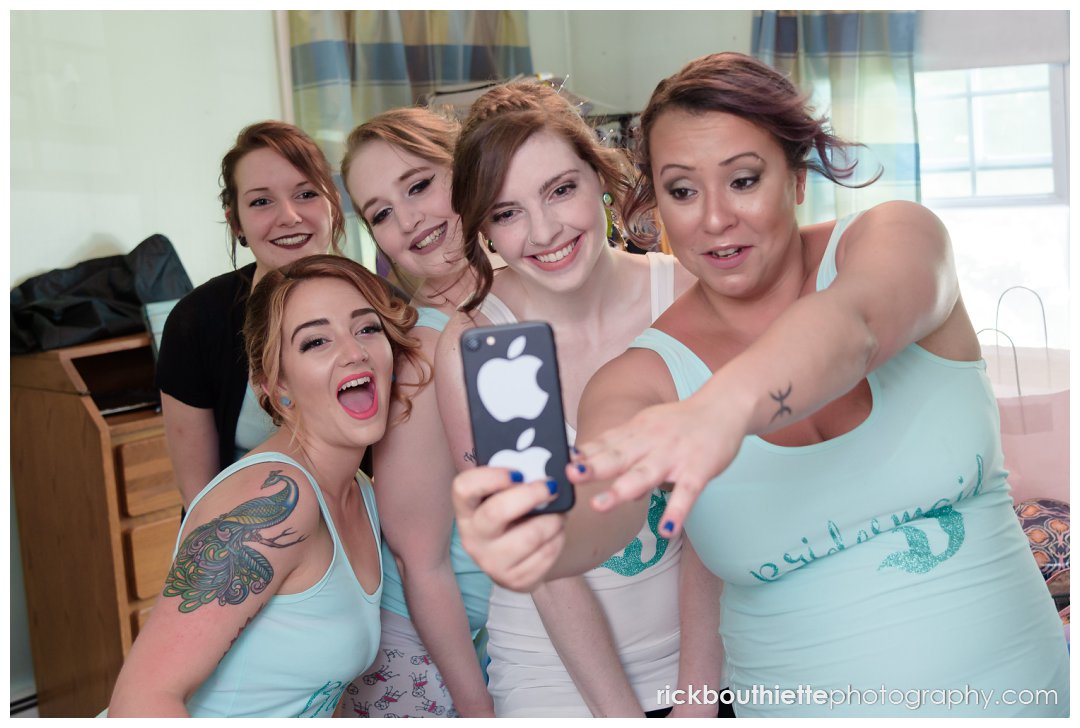 bride and bridesmaids take a selfie before getting dressed for New Hampshire backyard summer wedding