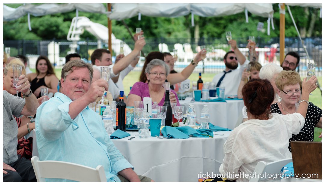 guests raise their glasses as they toast the bride and groom at New Hampshire backyard summer wedding reception