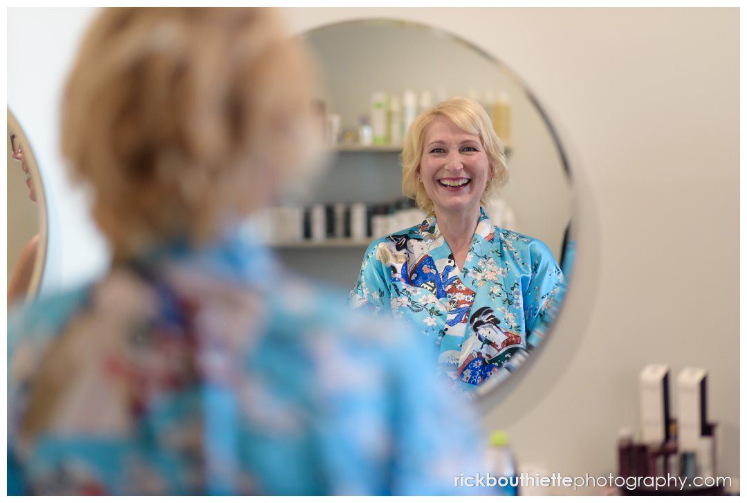 happy bride in mirror after her makeup done for her Ordiorne Point Seacoast wedding
