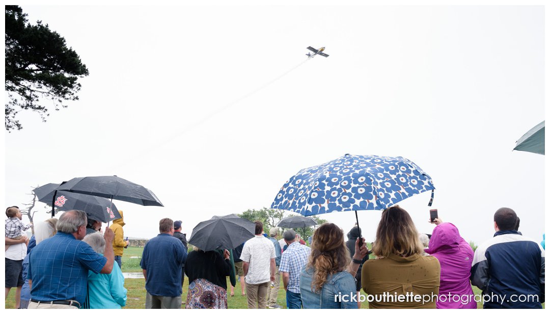 guests with umbrellas enjoy stunt plane overhead at Ordiorne Point Seacoast wedding reception