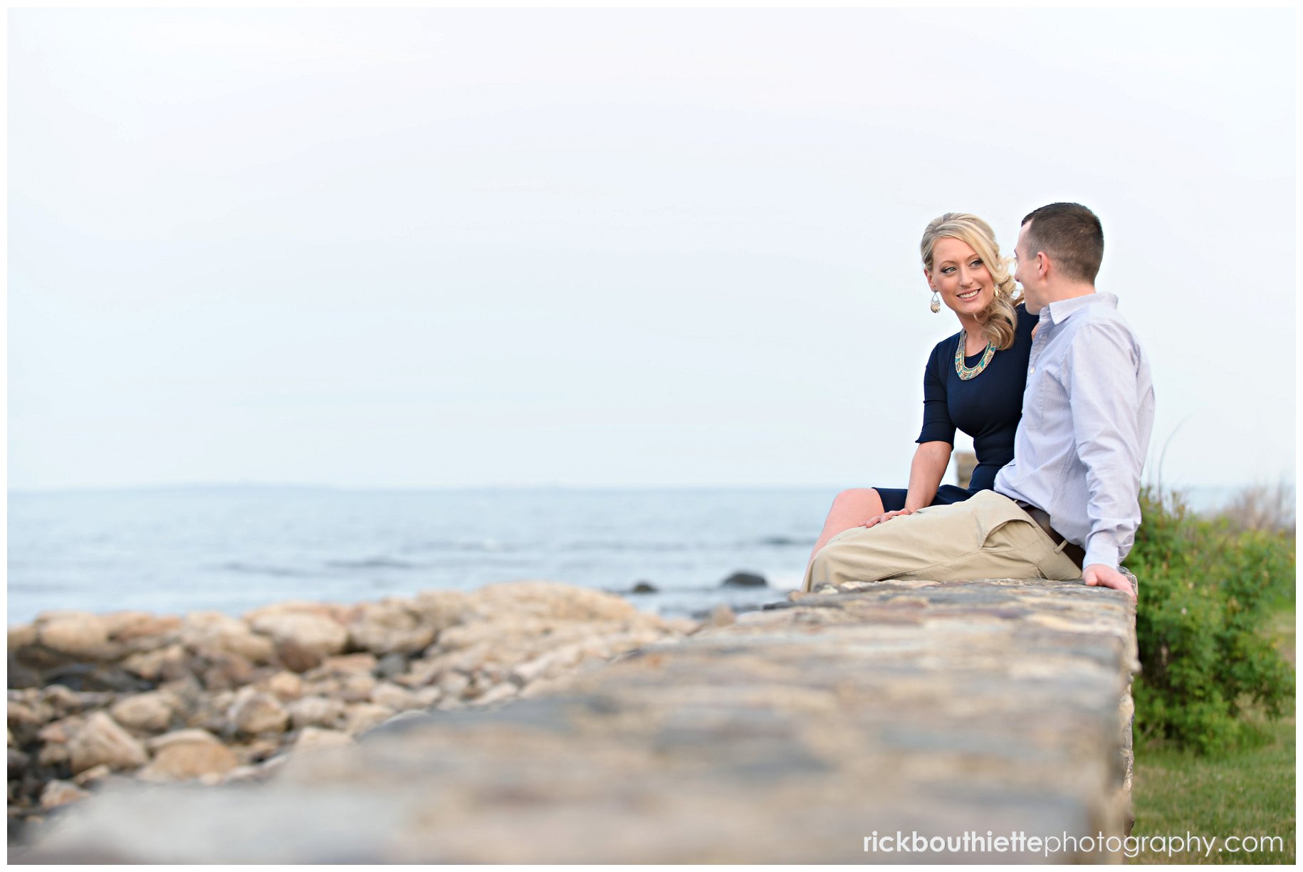 couple sitting on stone wallat Ordiorne Point engagement in Rye, NH